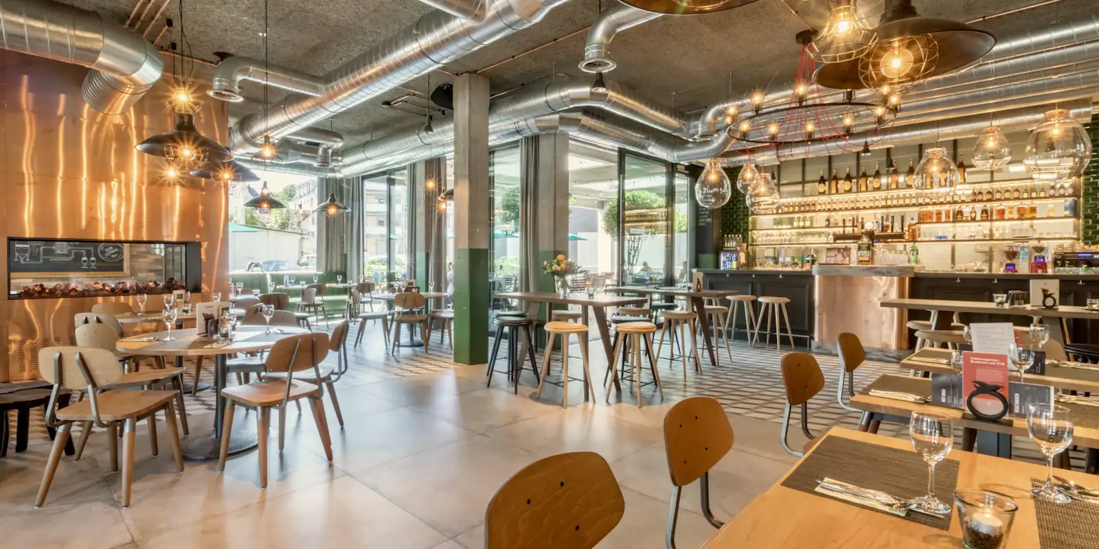 Světlá restaurace s dřevěnými stoly, barem a lampami.