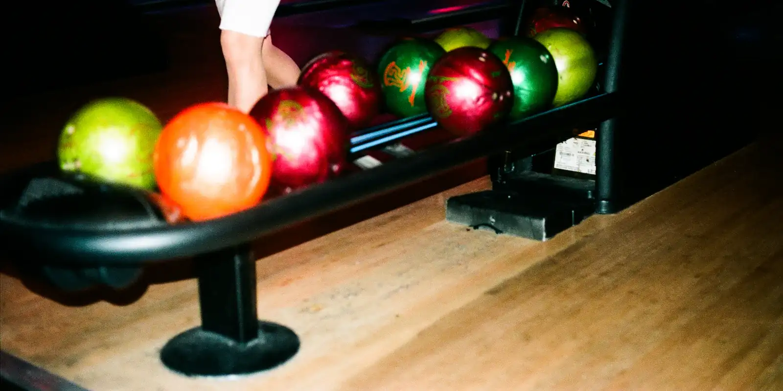 Barevné bowlingové koule v zásobníku u dráhy.