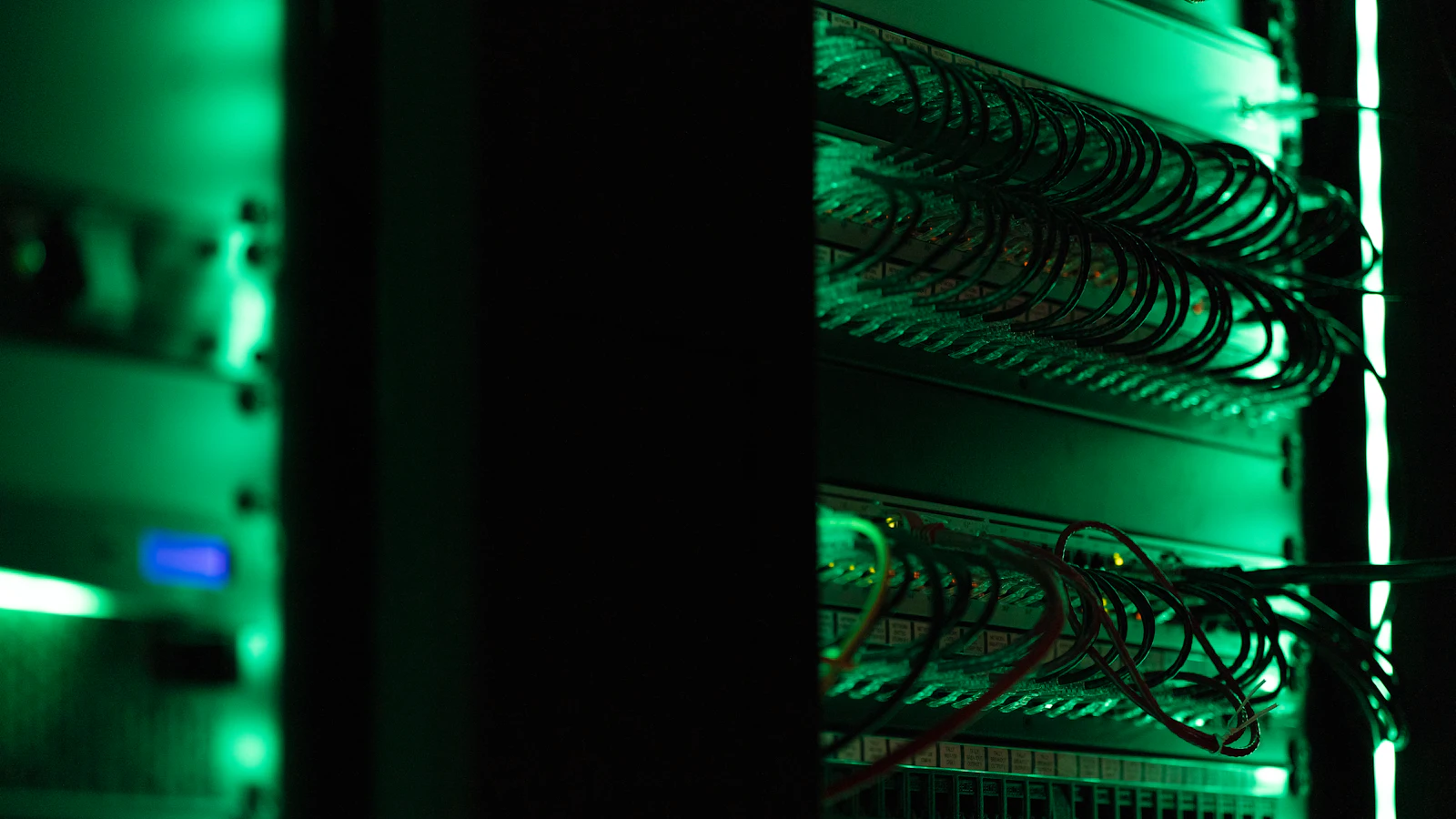 Serverový rack se zeleně podsvícenými síťovými kabely v tmavé serverovně.